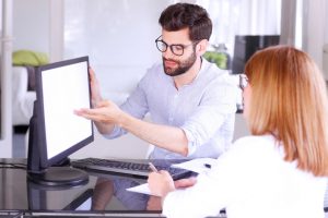 Portrait of group of business people consulting at office. Young businessman sitting in front of computer and points to the white screen while presenting his idea to mature businesswoman.
